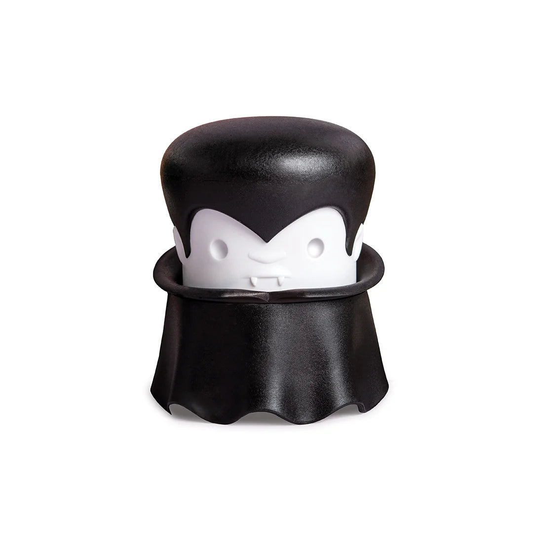 A cartoon vampire with a cape and fangs holds an OTOTO Gracula garlic crusher.