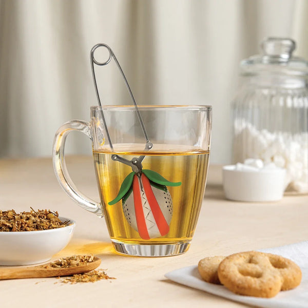 Glass mug with OTOTOs Tea Trap, a bowl of herbs, and cookies on the table.